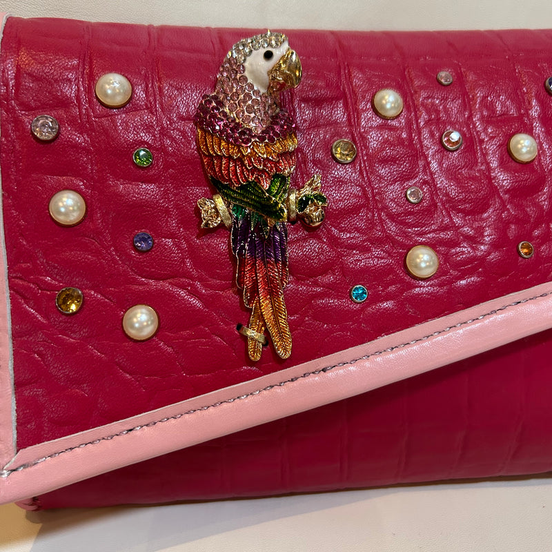 Close up of crystal accents and colorful crystal parrot embellished leather clutch in magenta pink. 